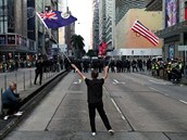 Demonstrující lovk mává vlajkami USA a vlajkou svobodného Hongkongu.