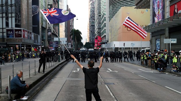 Demonstrující lovk mává vlajkami USA a vlajkou svobodného Hongkongu.
