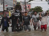 Místní peváí mue na motorce zaplavenou tvrtí na okraji Jakarty.