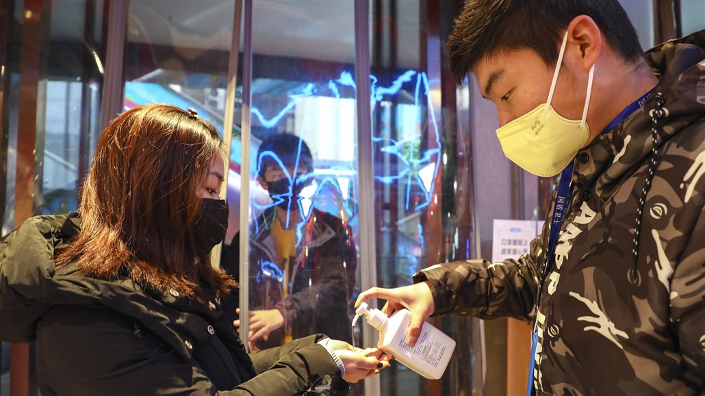 Pracovník obchodu v mst Wu-Chan dávkuje lidem u vchodu dezinfekci.