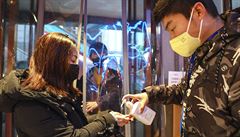 Pracovník obchodu v městě Wu-Chan dávkuje lidem u vchodu dezinfekci.
