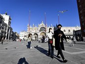 Turisté s roukami kráejí po benátském námstí sv. Marka.
