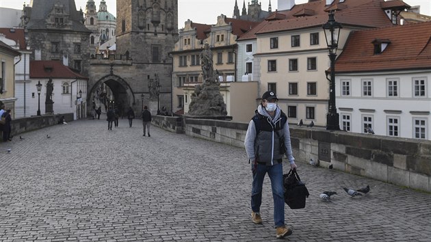 Mu s ochrannou maskou na oblieji prochází po Karlov most v Praze.