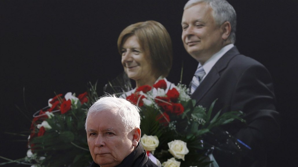 Jarosław Kaczyński s fotkou svého bratra a jeho manželky v pozadí.