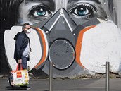 Mu s respirátorem prochází kolem koronavirového graffiti v italském Milánu.