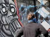 Mu s roukou prochází okolo graffiti masky v rakouském hlavním mst Vídni.