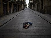 Bezdomovec spí uprosted vyprázdnné barcelonské ulice.