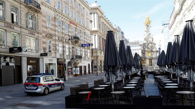 Policejní vz projídí kolem prázdných zahrádek restaurací v centru Vídn.