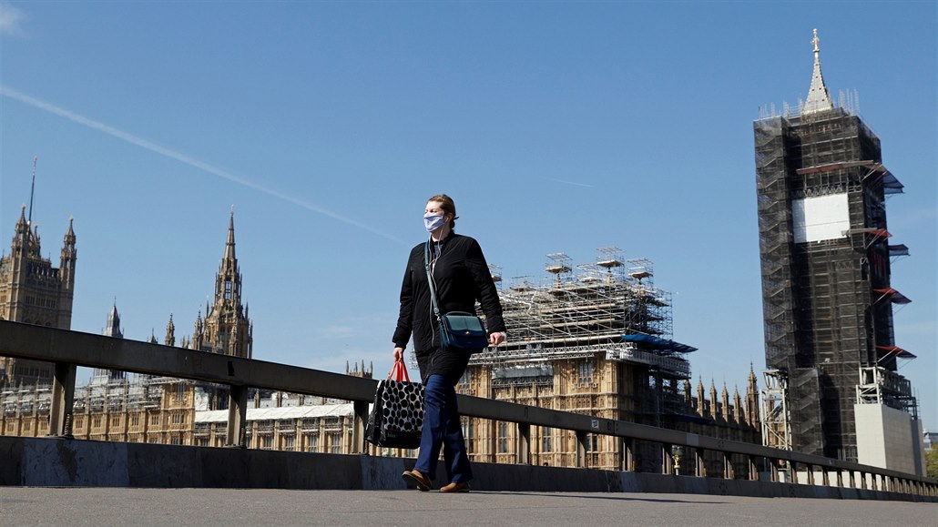 Žena s rouškou přechází westminsterský most v Londýně přes budovou britského...