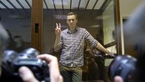Alexej Navalnyj pózuje fotografům zpoza skleněného boxu u soudu v Moskvě.