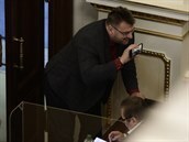Poslanci obehnaní plexisklem Marian Bojko a Lubomír Volný (s mobilem v ruce) ve...