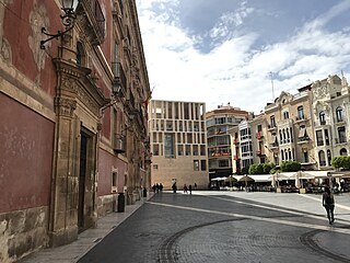Murcia, pohled na modern budovu ped stojc proti katedrle. Vlevo s ervenou...