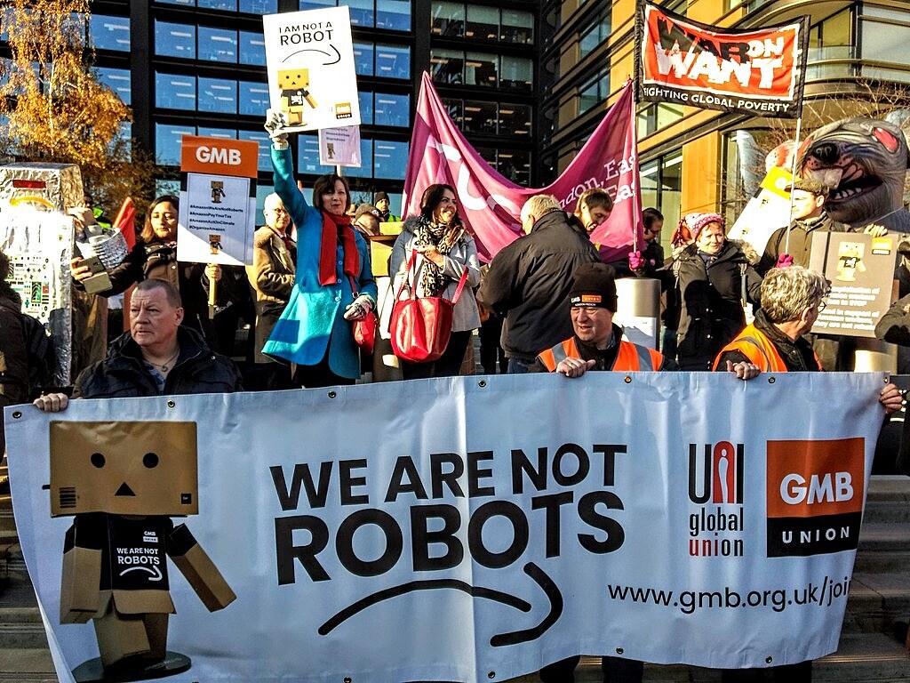 Protestující zaměstnanci Amazonu s transparantem „Nejsme roboti“.