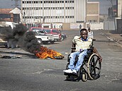 Protestující vozíká projídí okolo hoící pneumatiky v Johannesburgu.