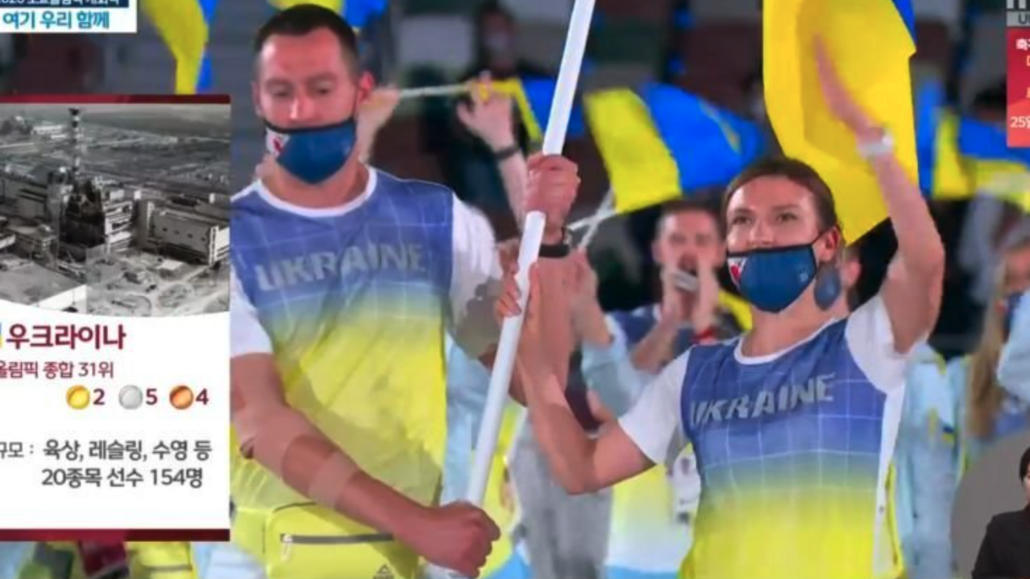 Ukrajinští vlajkonoši při zahájení olympiády v Tokiu s fotkou Černobylu na...