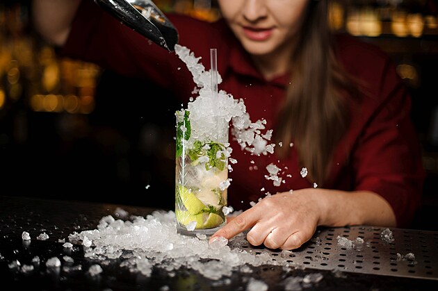 pretty barmaid in a red dress adds to mojito in a crystal glass crushed ice...