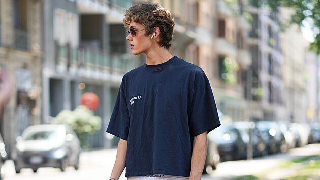 MIL�N, IT�LIE � 20. �ervna: Model m� kr�tk� kudrnat� hn�d� vlasy, kulat� zlat� slune�n� br�le s tmav�mi skly, tmav� modr� oversized tri�ko s kr�tk�m ruk�vem a kulat�m v�st�ihem, b�ov� �irok� �ortky ke kolen�m s �ed�mi postrann�mi pruhy, st��brn� n�ramek a modr� �abky. V ruce dr�� chytr� telefon. Sn�mek byl po��zen p�ed p�ehl�dkou Dolce & Gabbana b�hem mil�nsk�ho t�dne p�nsk� m�dy pro kolekci jaro/l�to 2027 dne 20. �ervna 2026 v Mil�n� v It�lii. (Foto: Edward Berthelot/Getty Images)