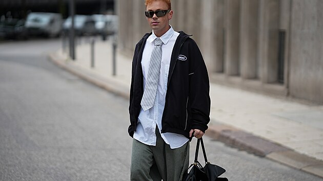 Erik Scholz je zachycen v �ern� oversized sportovn� bund� na zip zna�ky Balenciaga s b�l�m lemov�n�m, vy�it�m logem na hrudi a elastick�mi p�sky v pase a na ruk�vech; v b�l� oversized ko�ili Gus z pevn�ho bavln�n�ho popel�nu se �pi�at�m l�mcem od The Frankie Shop; v klasick� kravat� se st��brn�mi pruhy v tradi�n�m st�ihu od Calvin Klein; ve sv�tle modr�ch a b�ov�ch sepran�ch d��n�ch typu super baggy fit z kolekce 2023 se �irok�mi nohavicemi a extra dlouh�m st�ihem od Acne Studios; s �ernou kabelkou Rodeo st�edn� velikosti z hladk� telec� k��e se zlat�mi kovov�mi prvky a detailem z�mku od Balenciaga; v obd�ln�kov�ch slune�n�ch br�l�ch Gascan s matn� �ern�mi obrou�kami a �ern�mi t�novan�mi skly od Oakley; a se �lut�m zlat�m prstenem Juste un Clou od Cartier, 22. �ervence 2025.