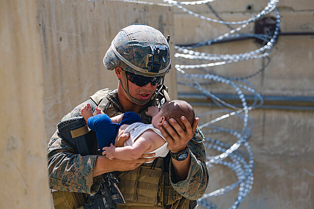 Americký mariňák utišuje afghánského kojence, zatímco jeho matka prochází...